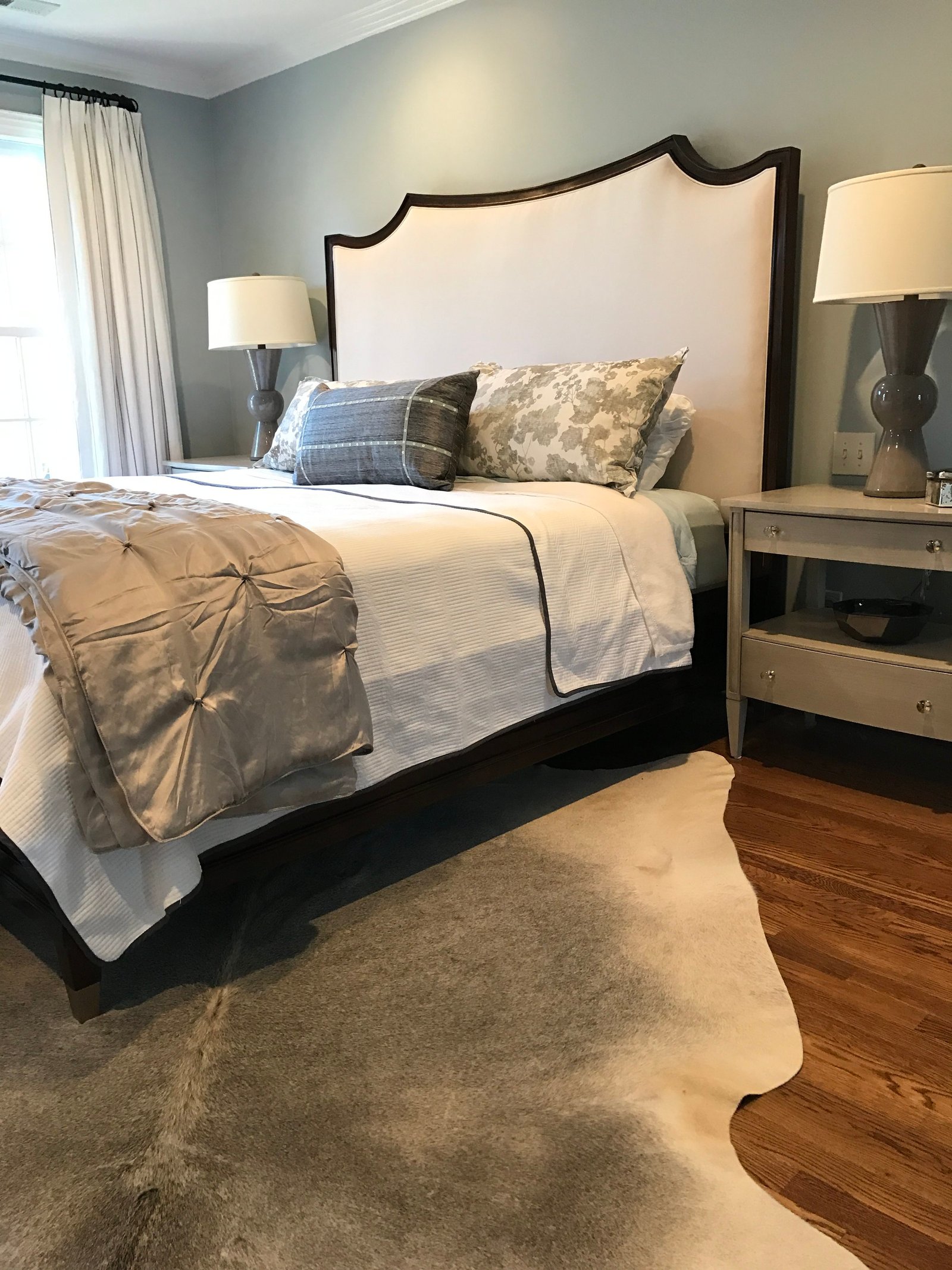 Serene bedroom with an arched upholstered headboard, silver bedding and a cowhide rug