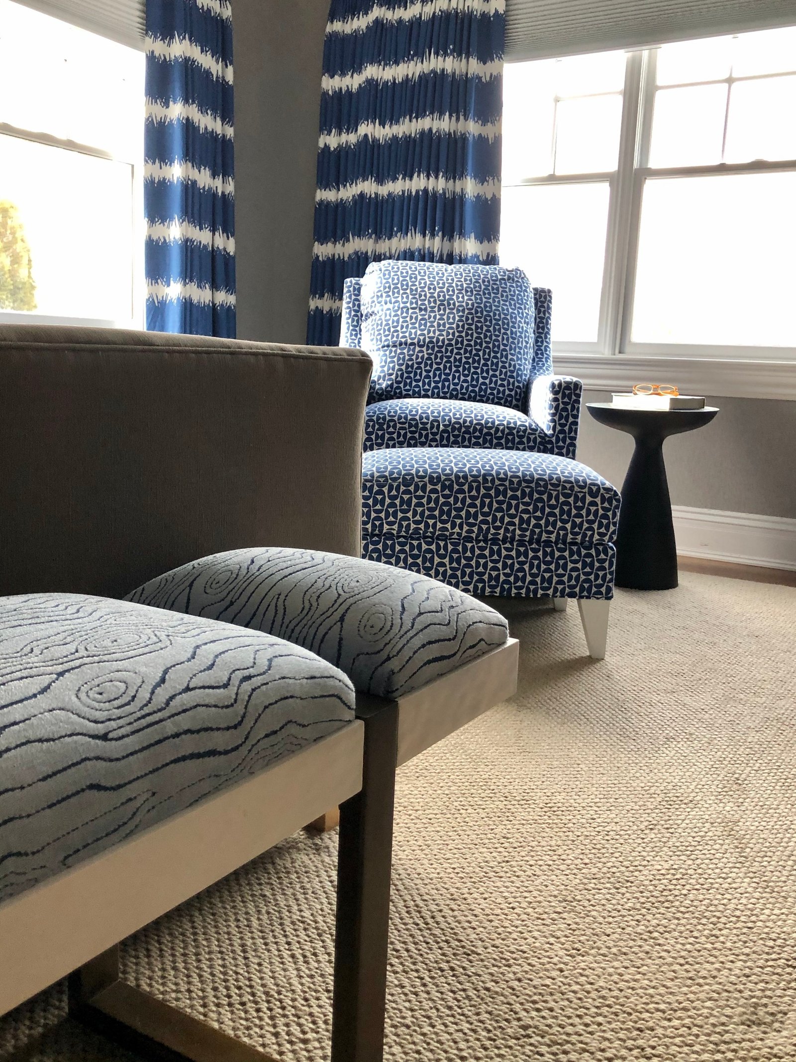 Upholstered bench with a wave-pattern cushion at the foot of the bed, a blue armchair by the window beyond