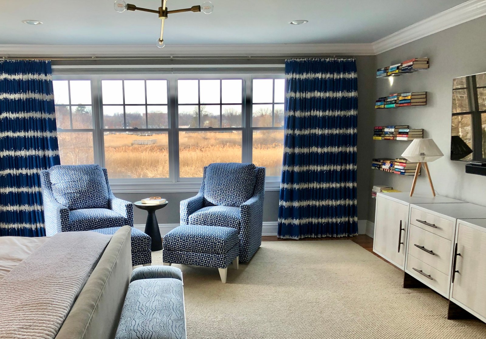 Coastal primary suite sitting area with blue patterned lounge chairs, ikat drapery and a view across the marsh