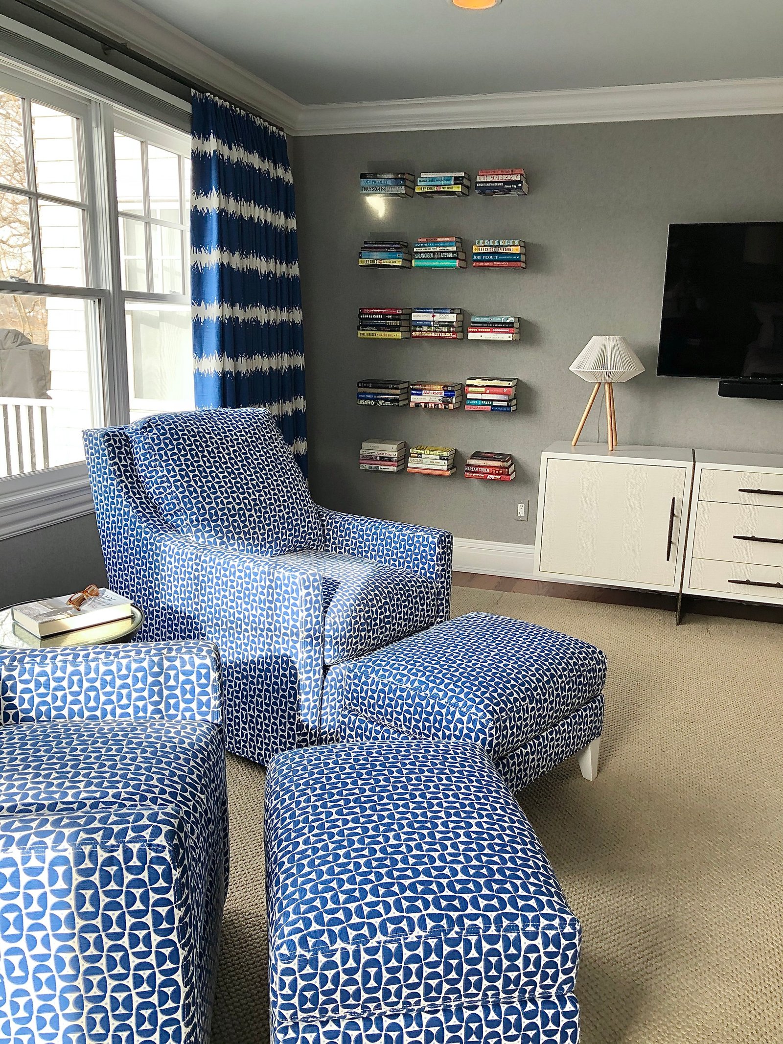 Blue patterned armchair and ottomans beside floating bookshelves stacked with books