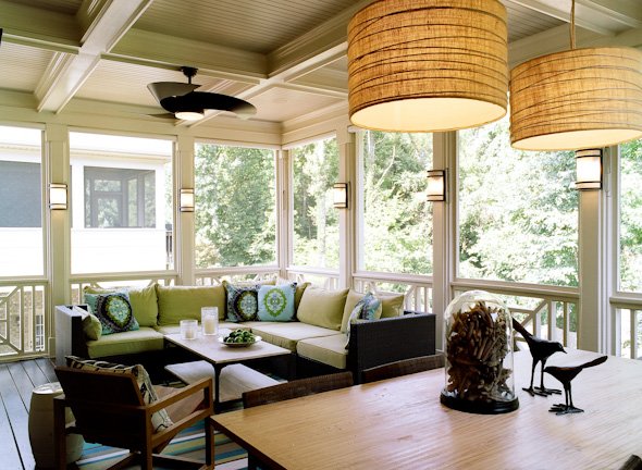 Screened porch with a green-cushioned sectional, oversized woven drum pendants and a wood dining table with a cloche and bird sculptures
