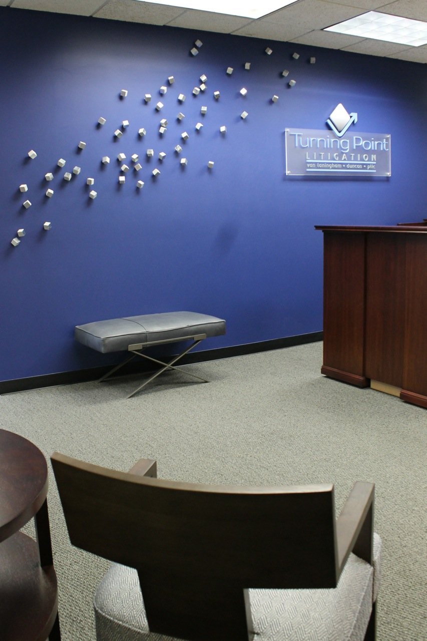 Turning Point Litigation reception with a cascade of silver cubes on a blue wall, a cherry reception desk and a gray upholstered bench