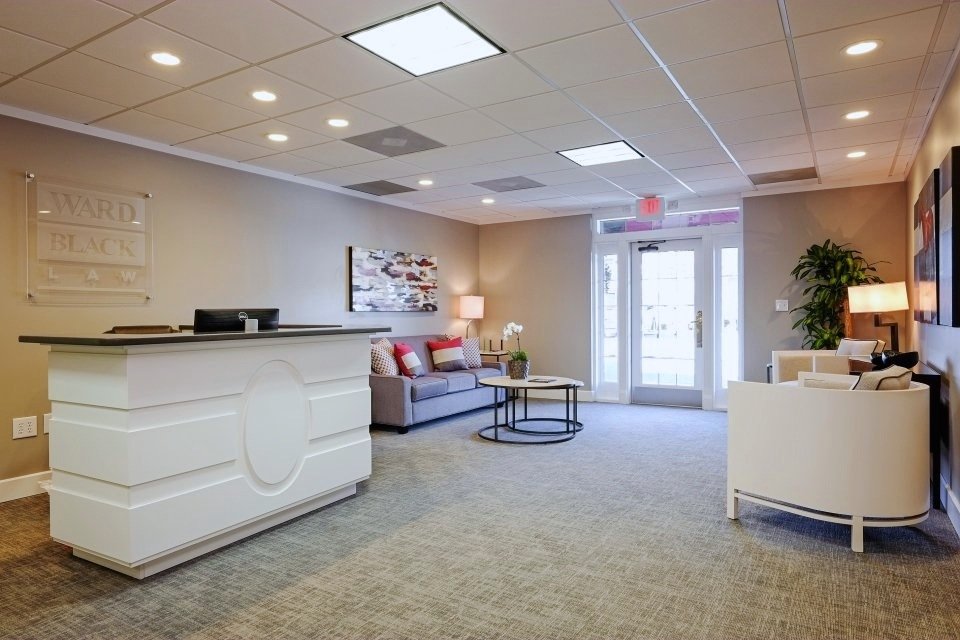 Ward Black Law reception with a white oval-detailed desk, gray sofa with red accent pillows and a cream curved armchair
