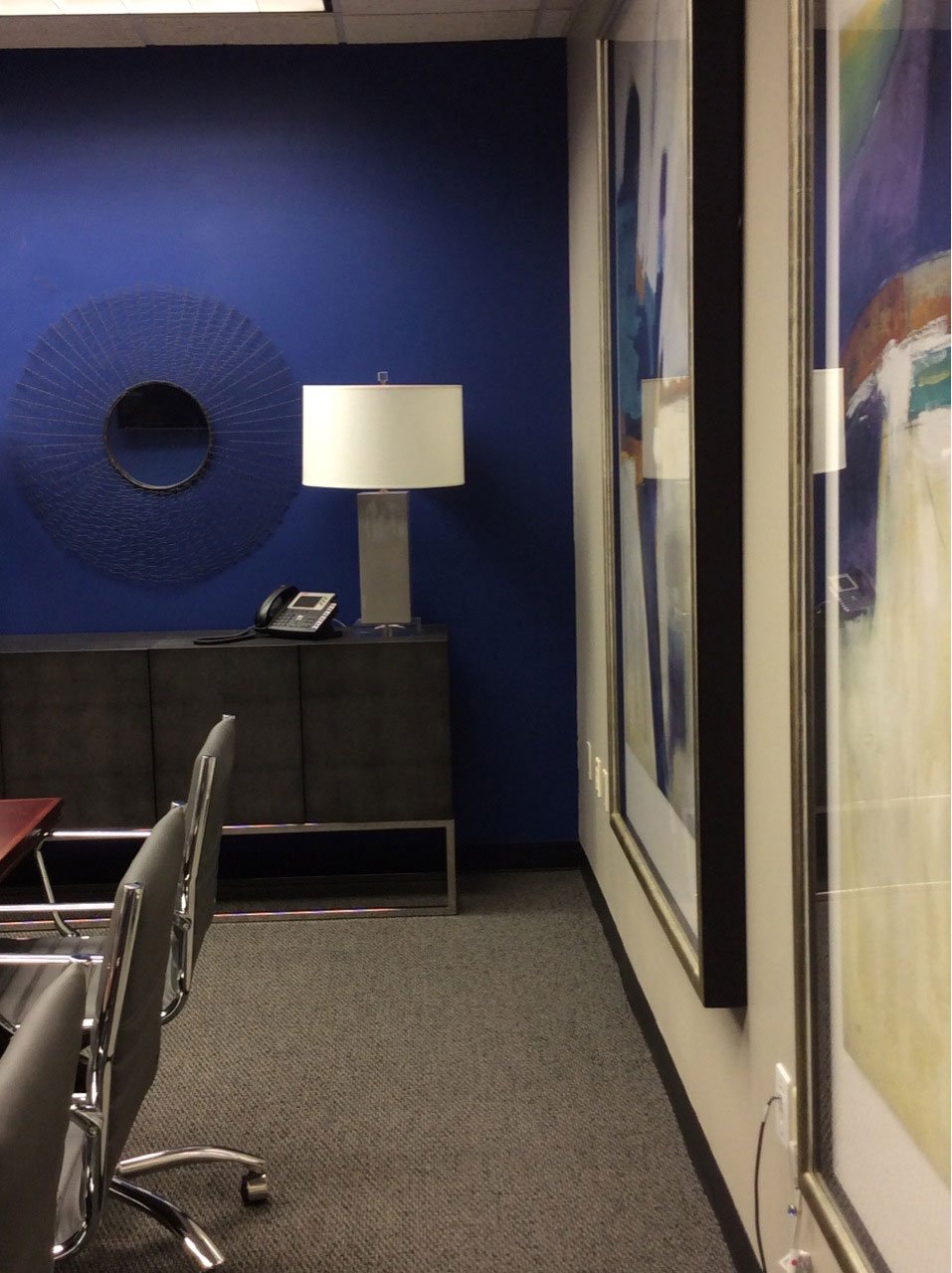 Conference room corner with a blue accent wall, a round sunburst mirror and large abstract art