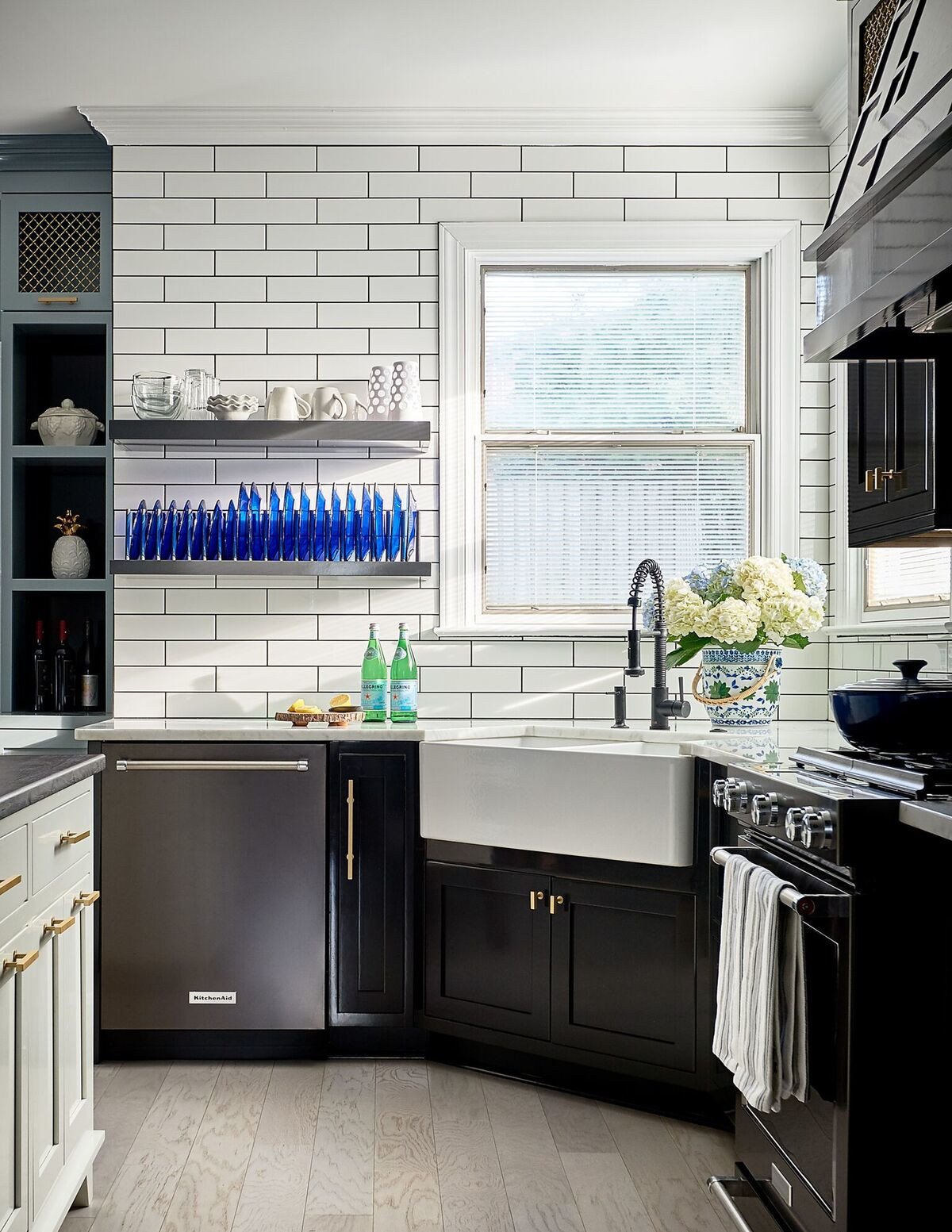 Kitchen with white subway tile, cobalt glassware on open shelves and an apron-front sink