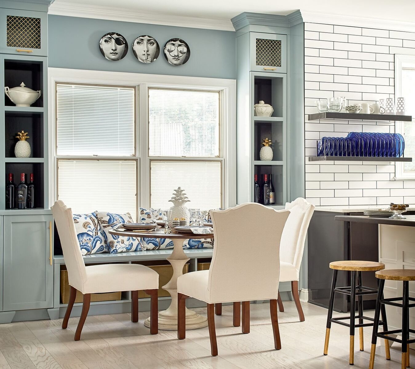 Breakfast banquette with blue-and-white cushions, cream wingback chairs and decorative face plates