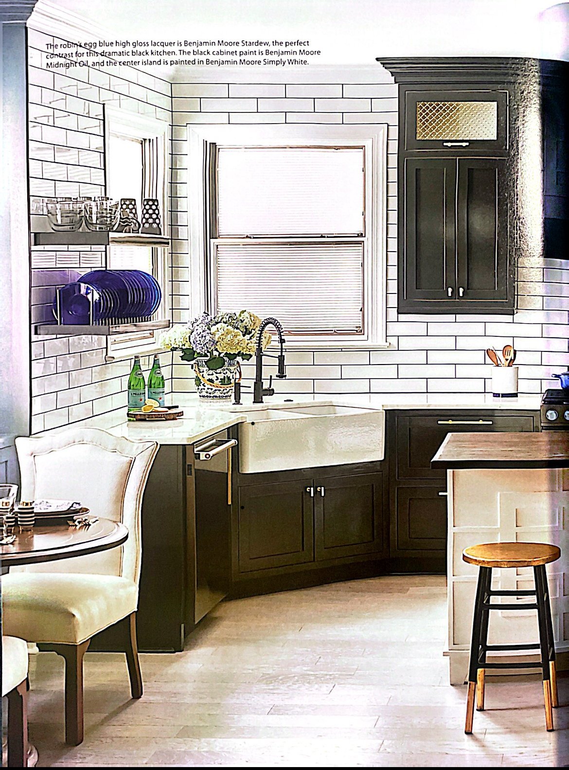 Magazine page showing a black kitchen with an apron-front sink, subway tile to the ceiling and open shelves of cobalt plates