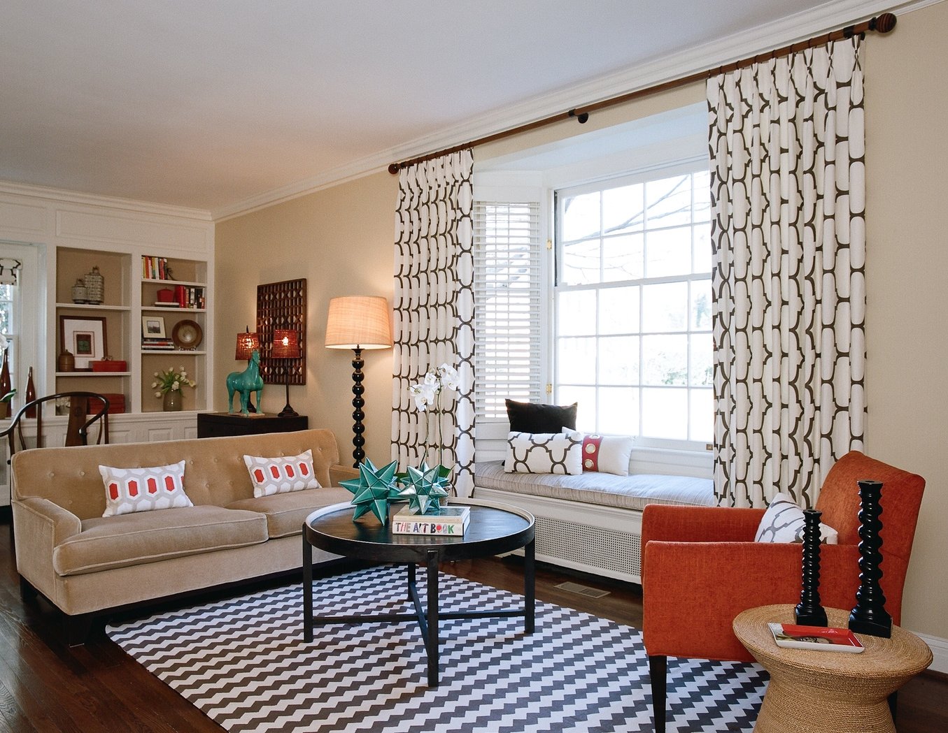 Living room with a black-and-white chevron rug, orange accent chair and patterned draperies