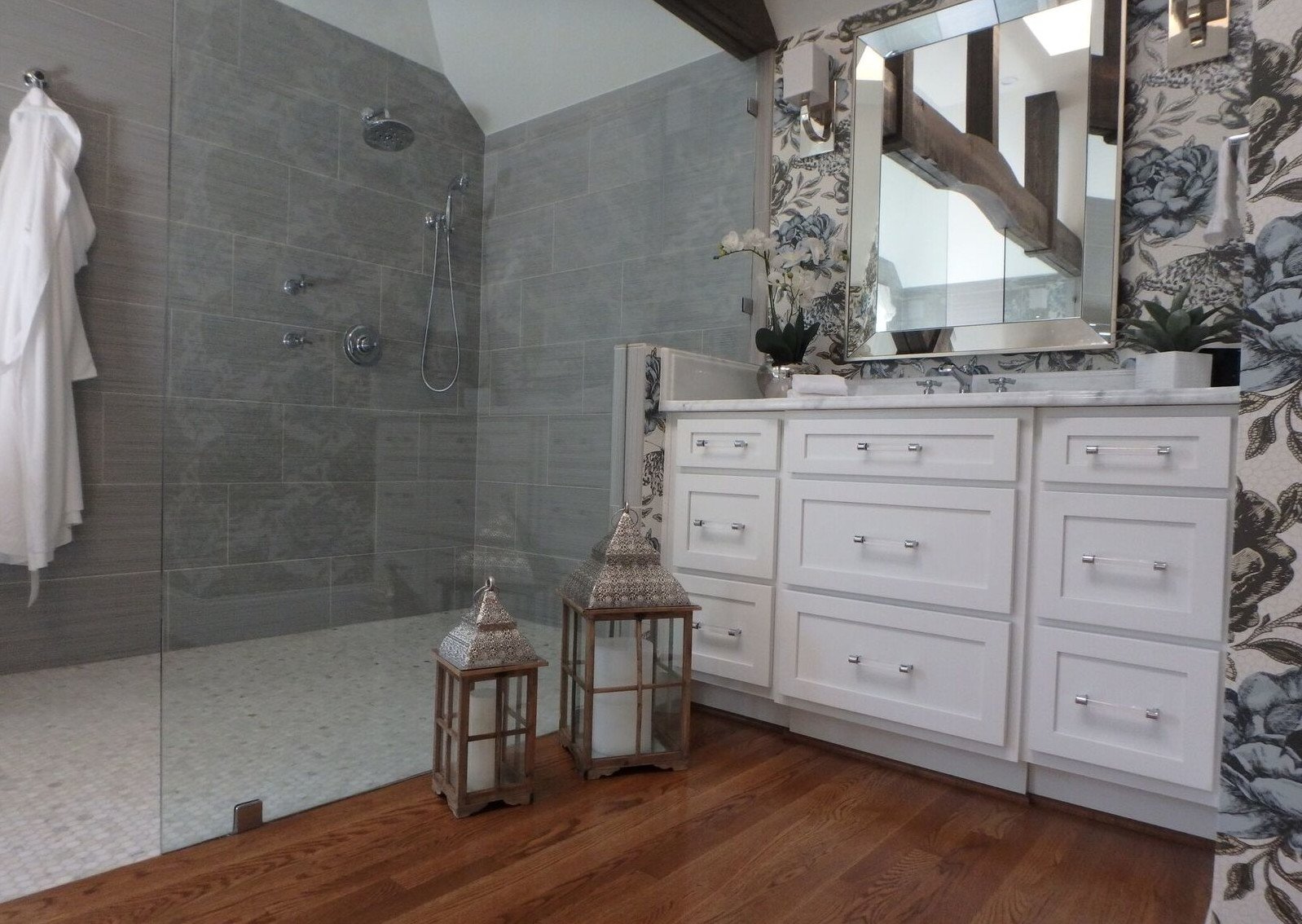 Walk-in shower beside a white vanity with lanterns and a mirrored frame