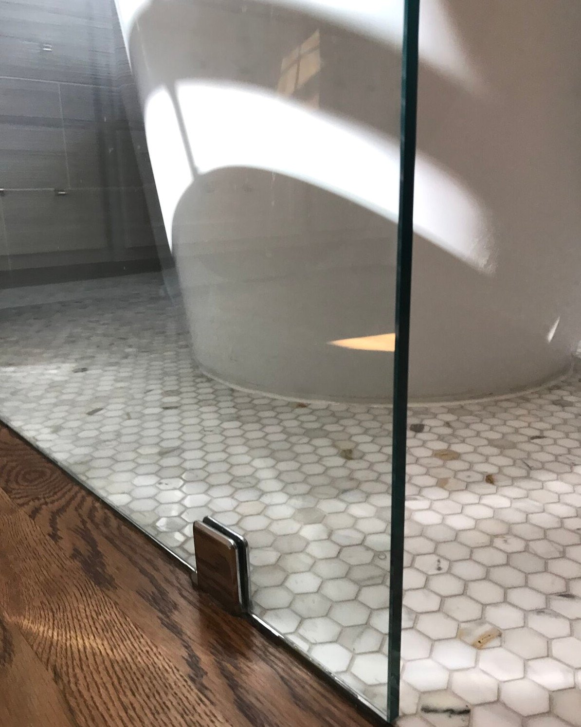 Hardwood meeting a marble hexagon mosaic floor at the glass shower enclosure