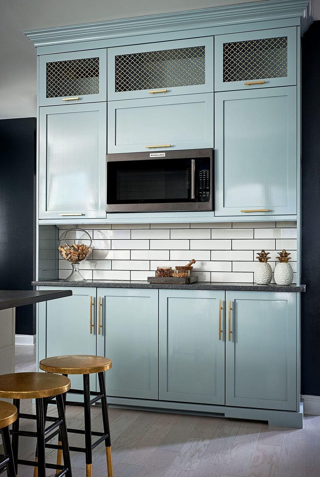 Pale blue-green pantry cabinetry with grille-front uppers, a built-in microwave and brass hardware