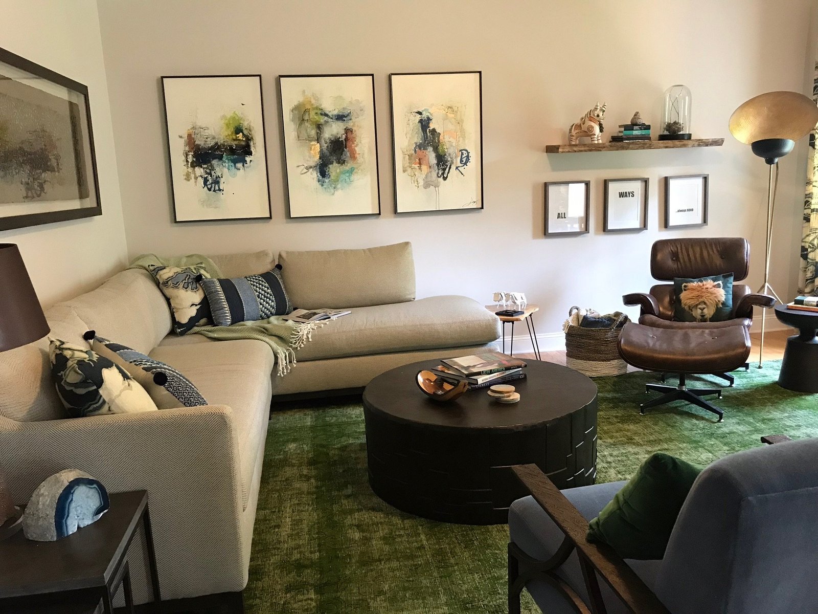 Living room with a cream sectional, emerald rug, leather lounge chair and a gallery of abstract art