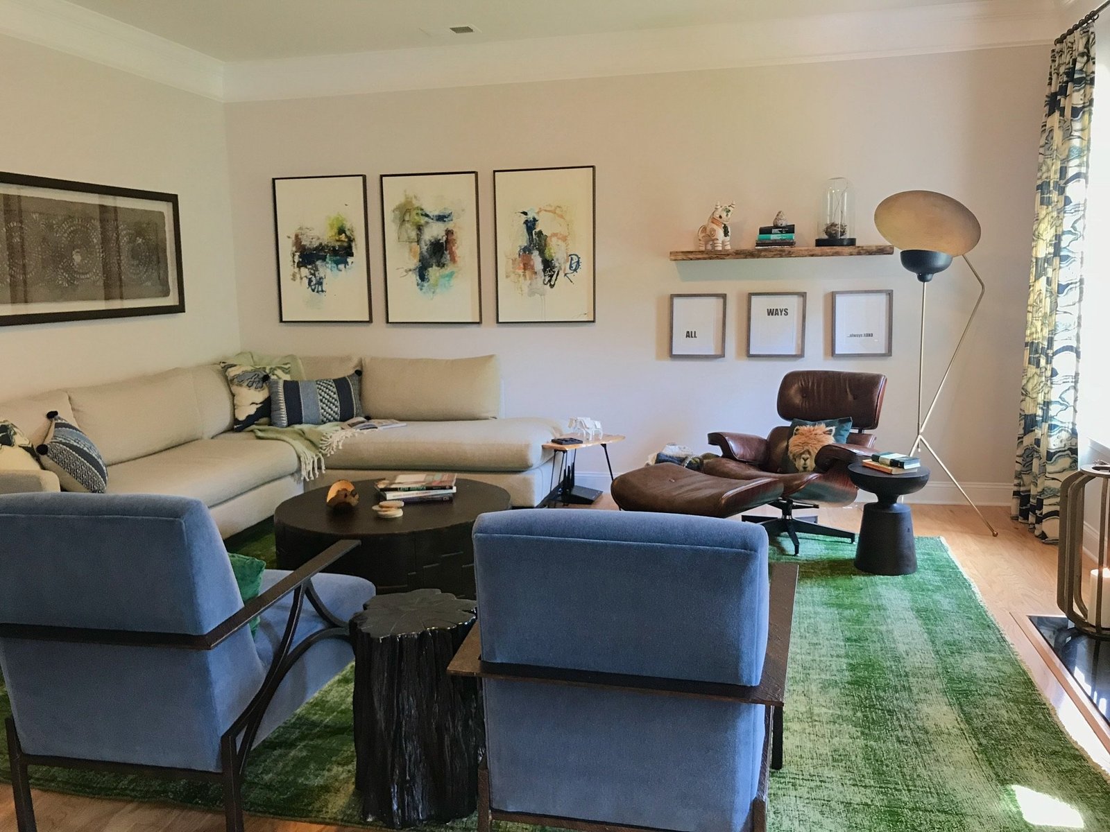 Living room with a cream sectional, blue velvet lounge chairs, an emerald rug and a gallery wall of abstract art