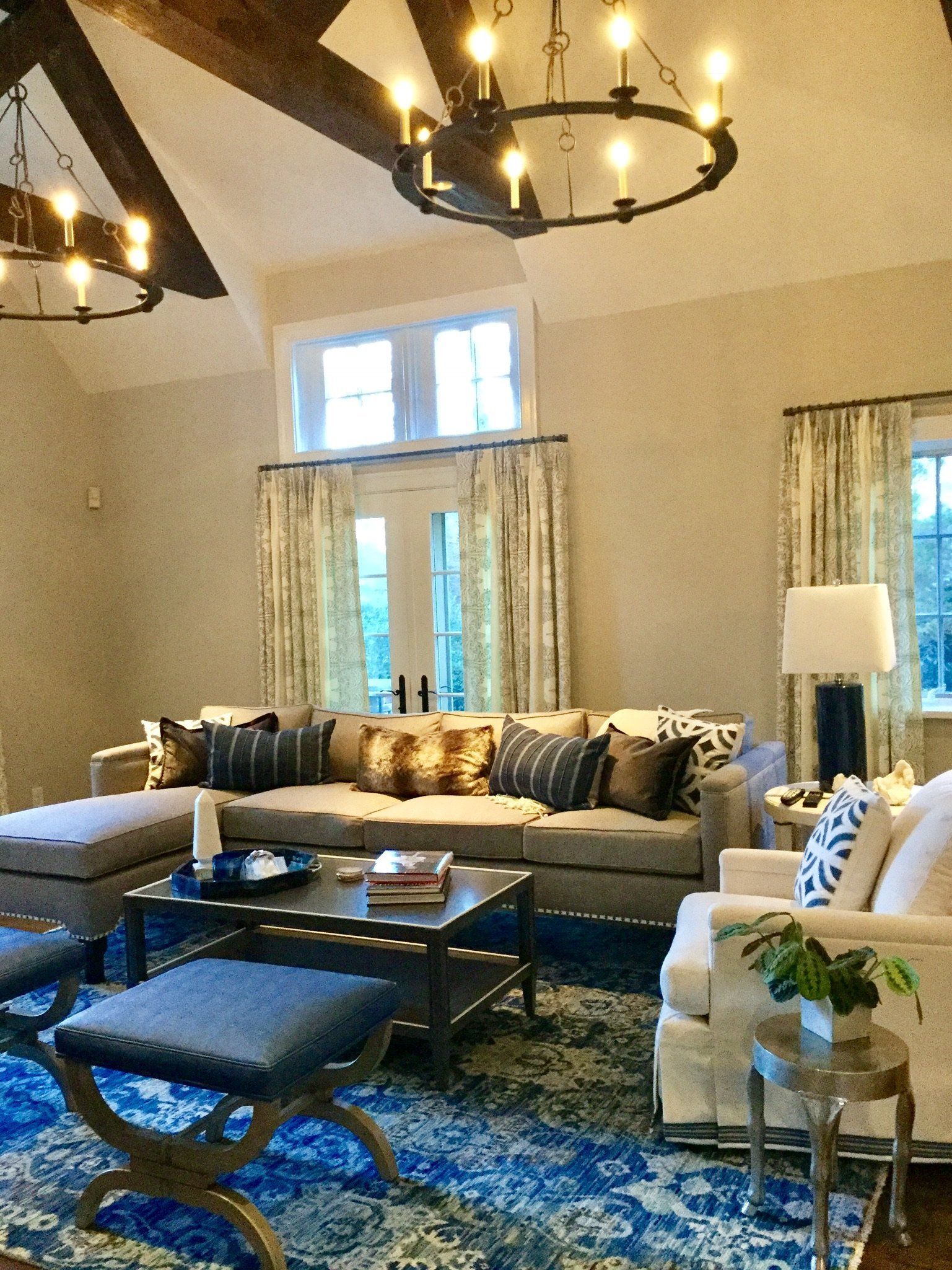 Living room with a ring chandelier, blue ottomans on a patterned rug and a deep sectional