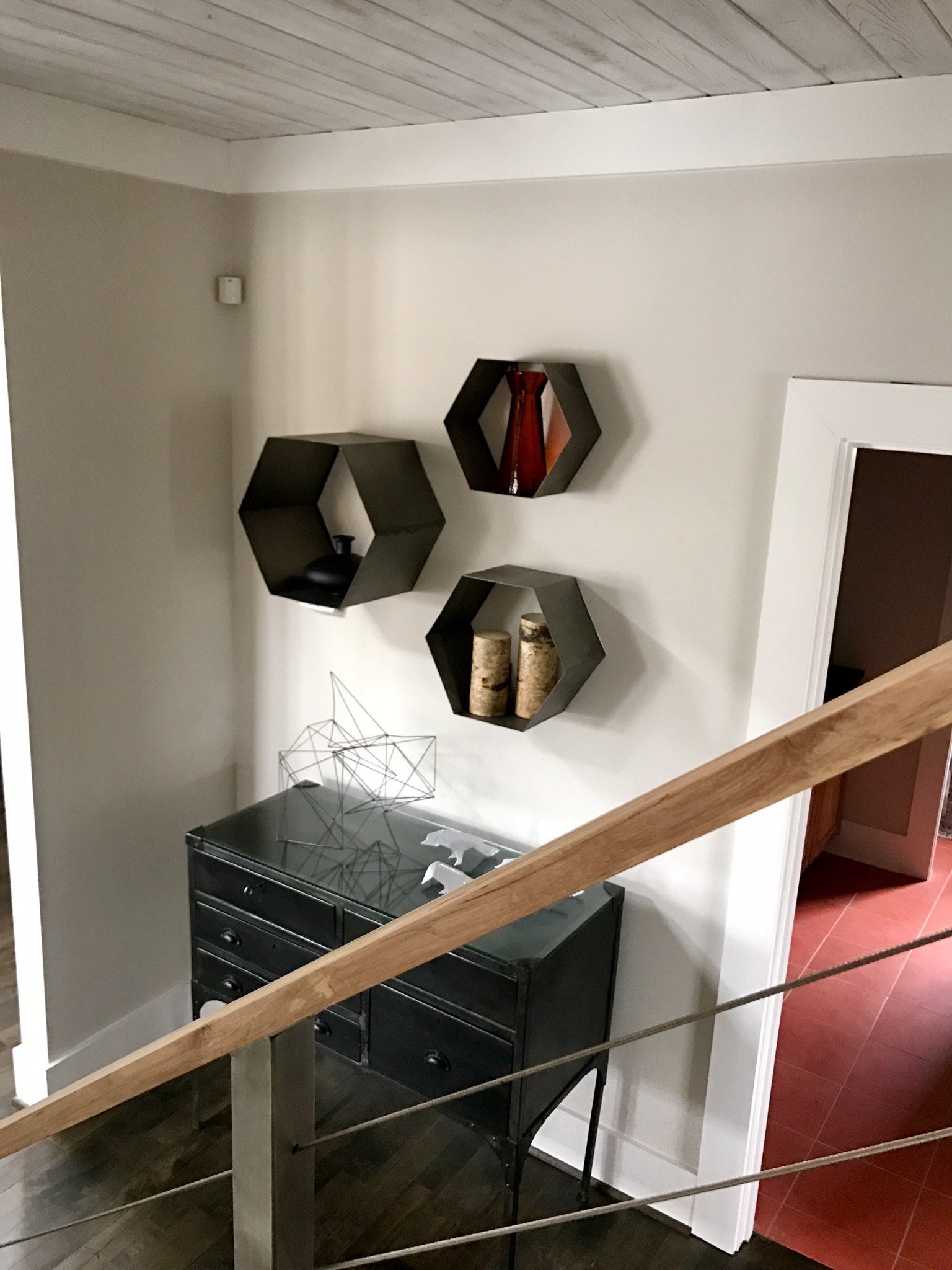 Stair landing with hexagonal wall shelves above a black chest and a wood and cable handrail