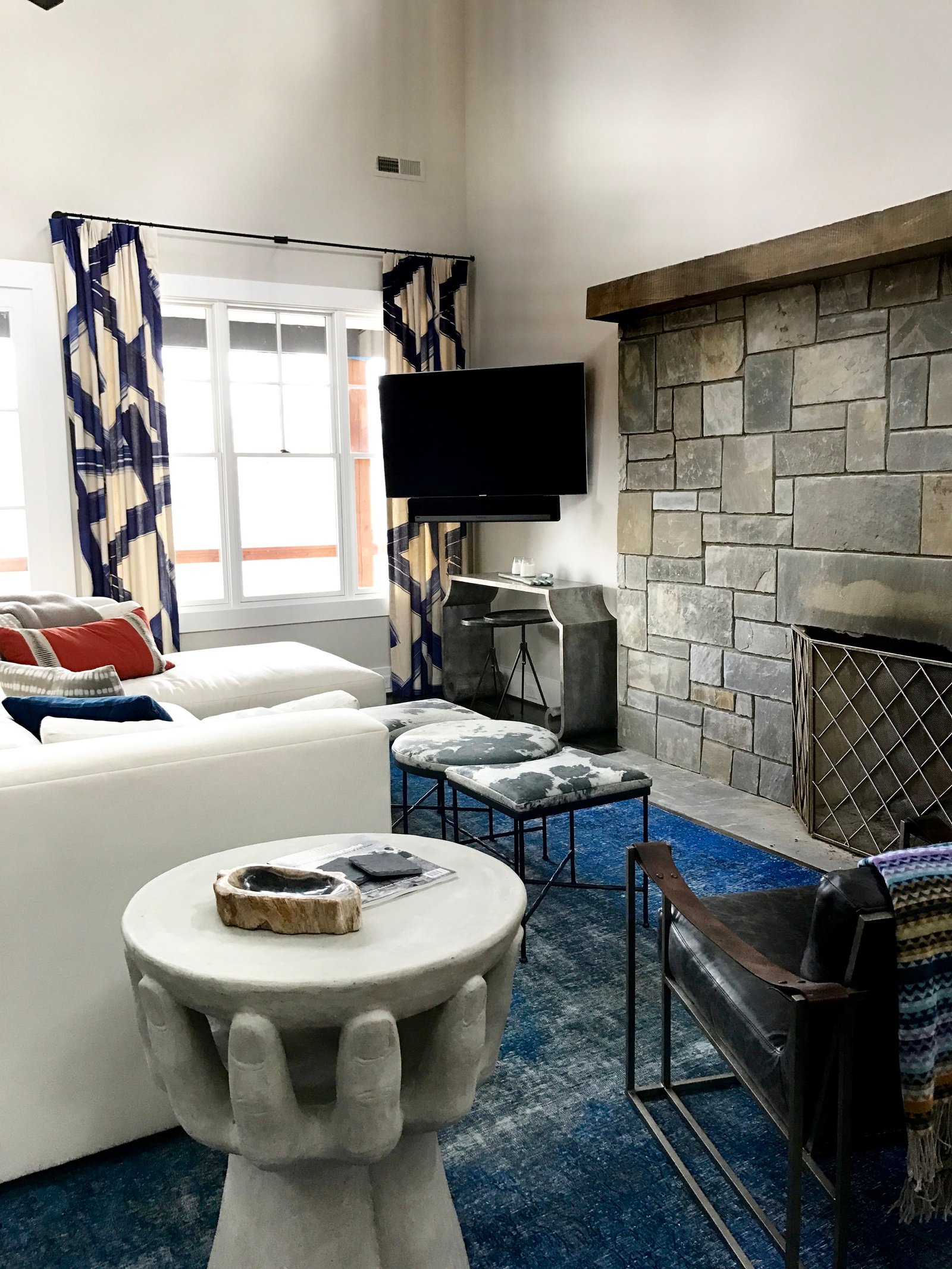 Great room with a sculptural hand side table, a white sectional, a stacked-stone fireplace, an indigo rug and ikat drapery