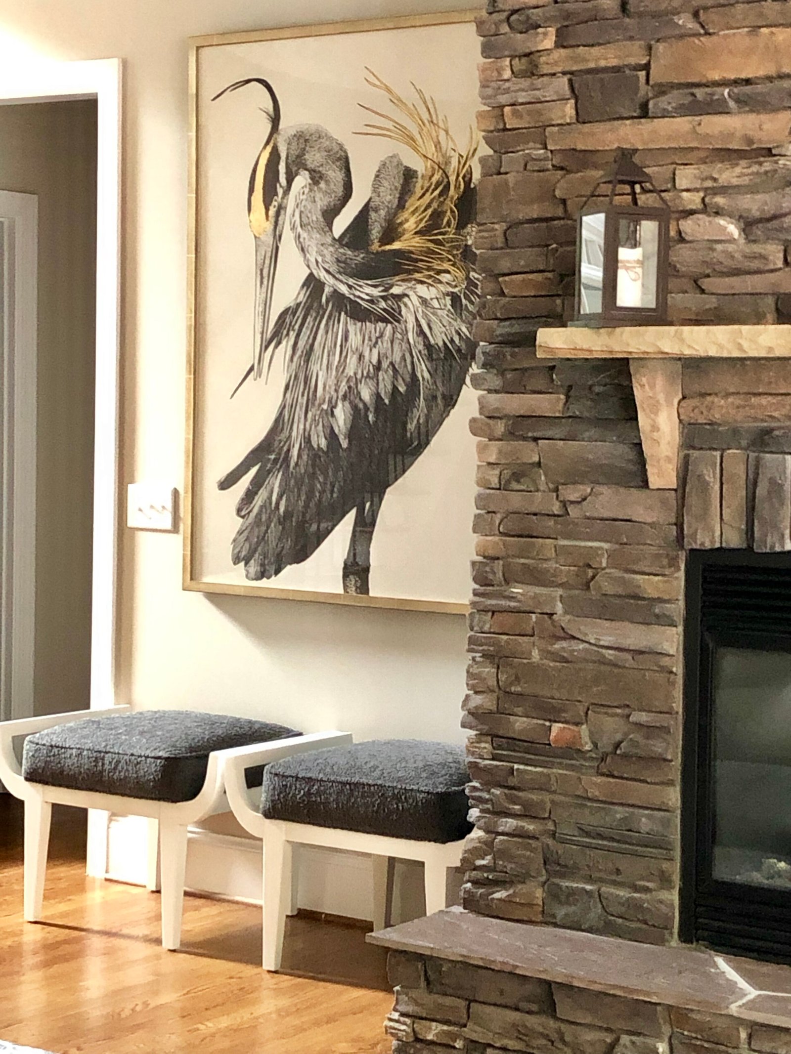 Living room with a large heron artwork beside a stacked-stone fireplace and a pair of upholstered benches