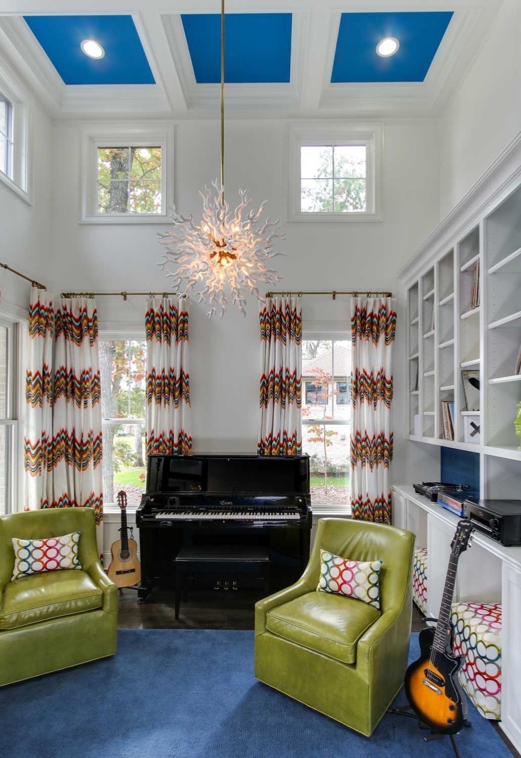 Double-height music room with a starburst chandelier, chartreuse club chairs and a black piano