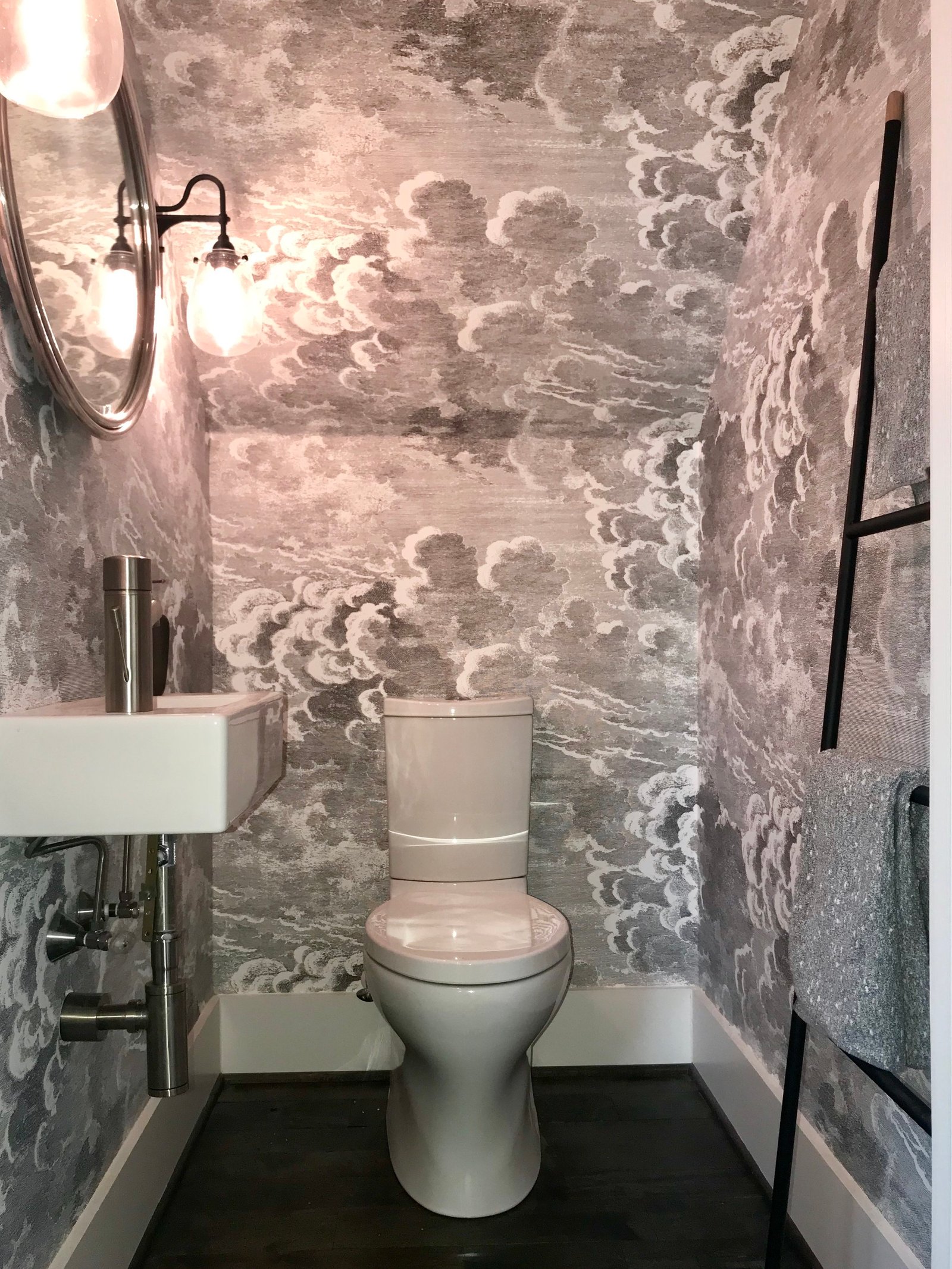 Powder room wrapped in dramatic black-and-white cloud wallpaper with a wall-mounted sink and round mirror