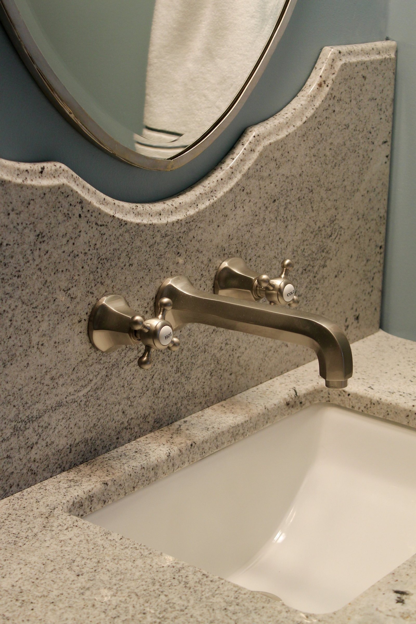 Wall-mounted cross-handle faucet in brushed nickel over a granite counter with a scalloped backsplash
