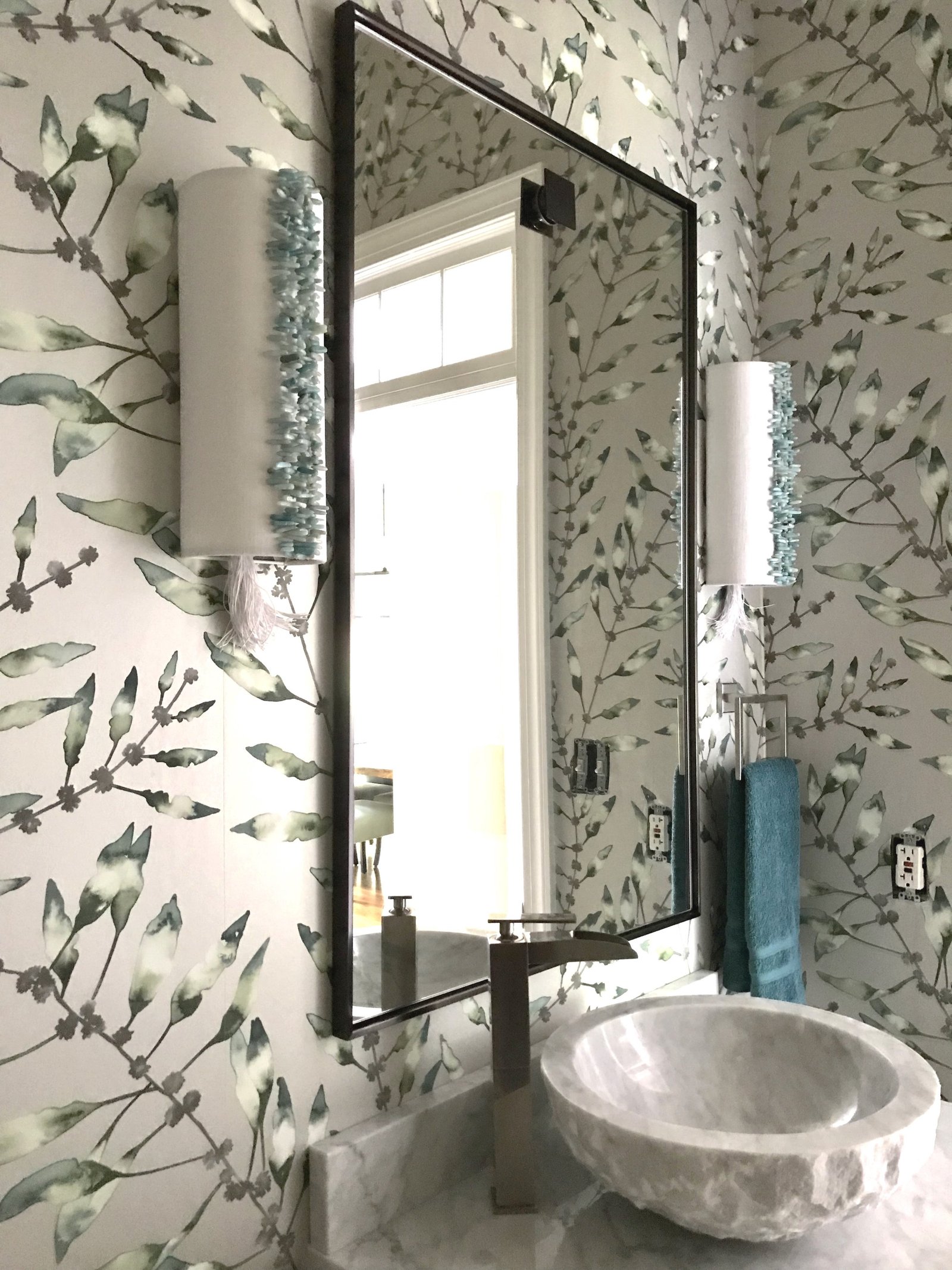 Powder room with botanical wallpaper, a carved stone vessel sink and a slim black-framed mirror
