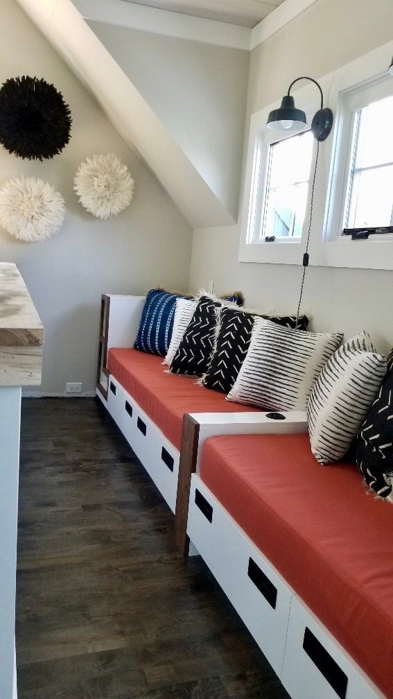 Long built-in window seat with coral cushions, black and white patterned pillows and woven wall hangings