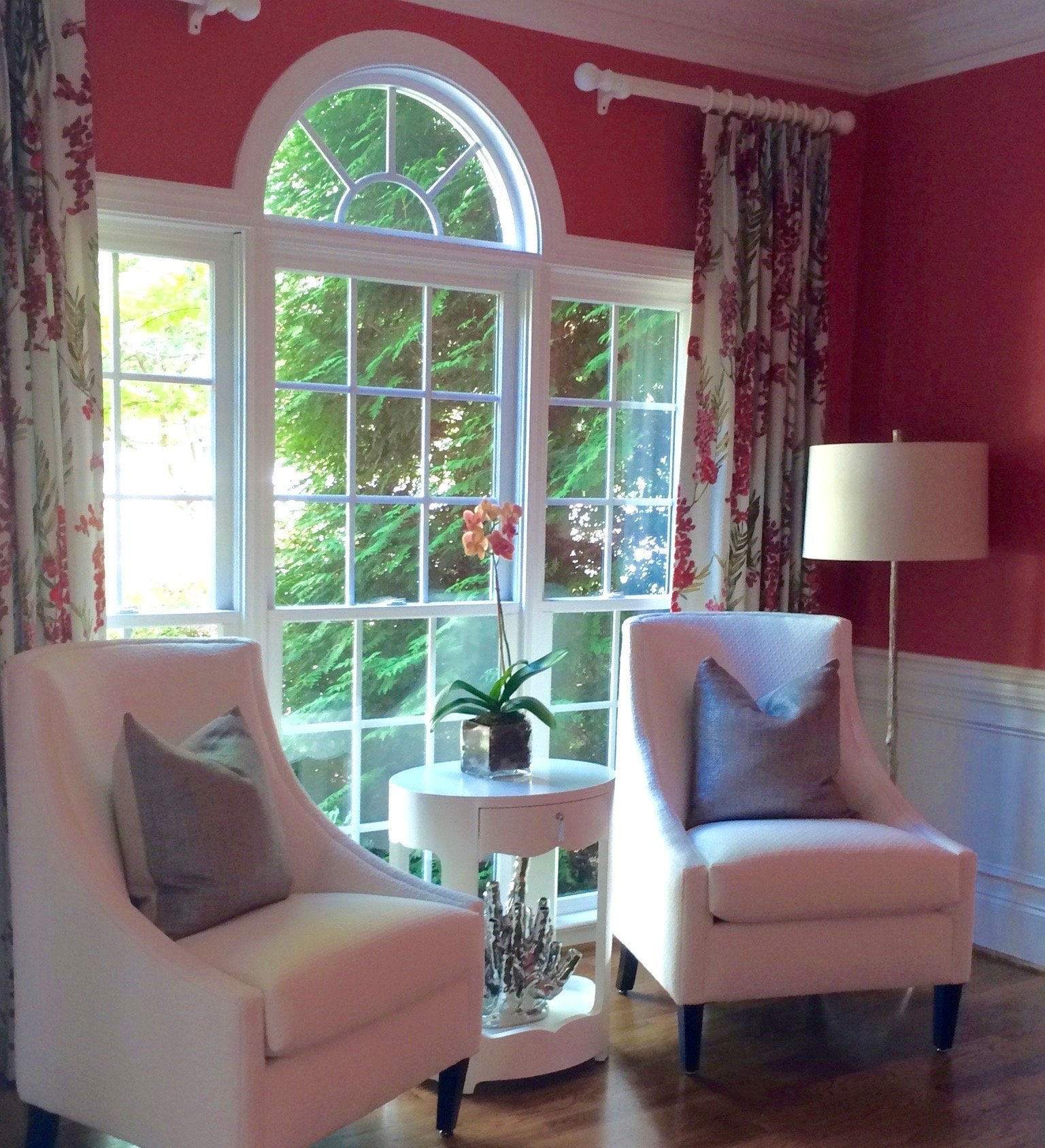 Sitting room with raspberry walls, an arched window, floral draperies and a pair of blush armchairs