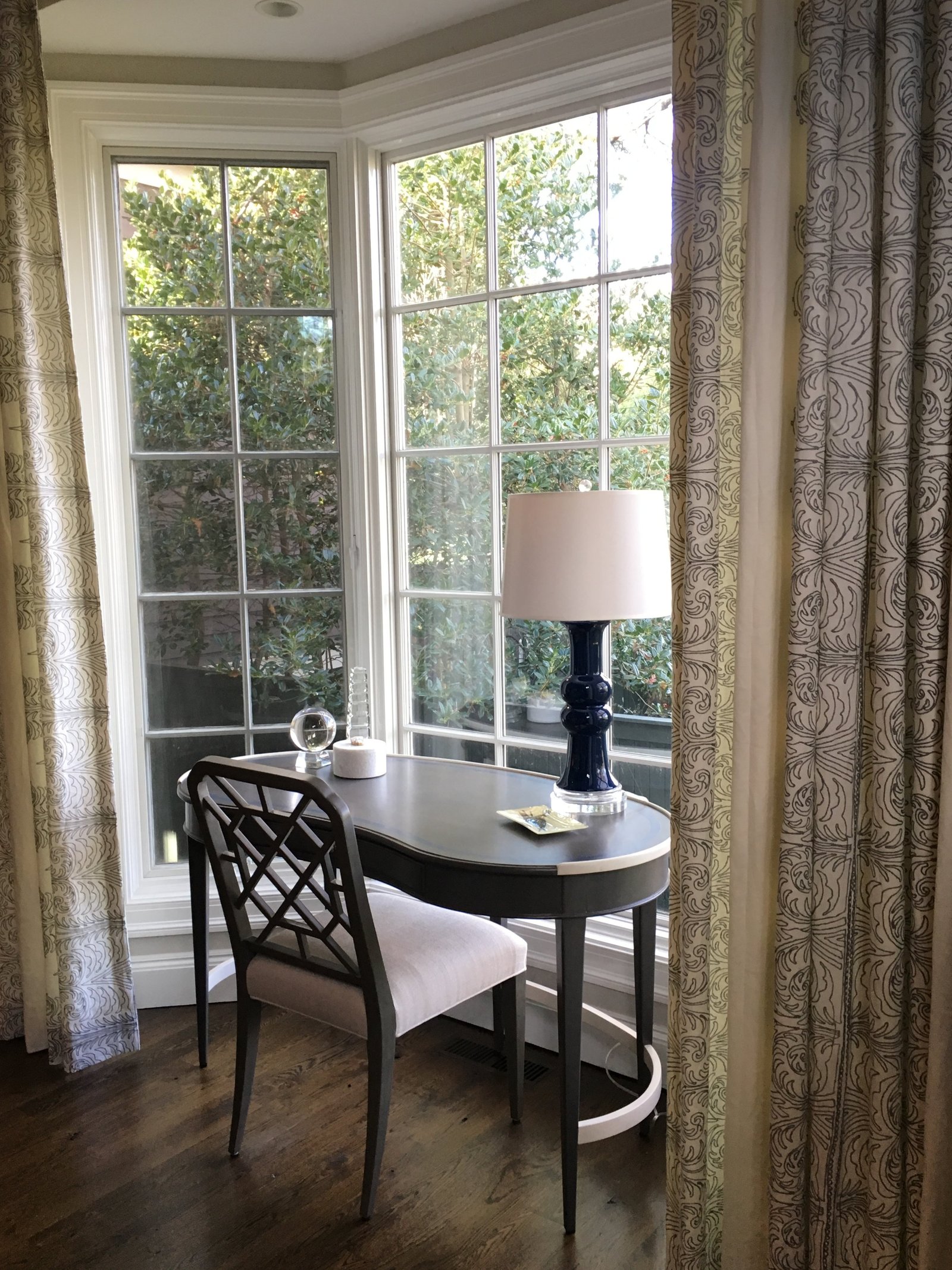 Writing desk and chair in a sunlit window bay framed by patterned drapery
