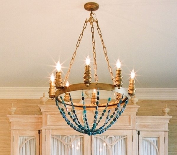Gilded candle chandelier strung with teal beads before the whitewashed armoire